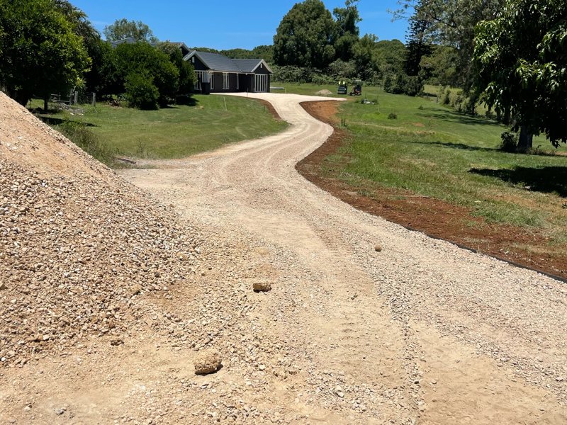Winding gravel driveway up to a new home, with a gravel stockpile in the foreground